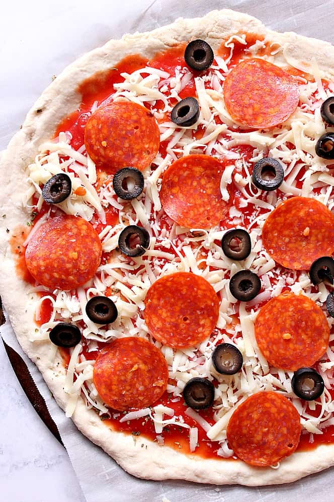 pizza dough with cheese, pepperoni and olives