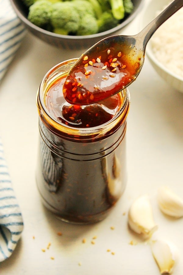 Homemade teriyaki sauce on a spoon over a jar, with sesame seeds visible.