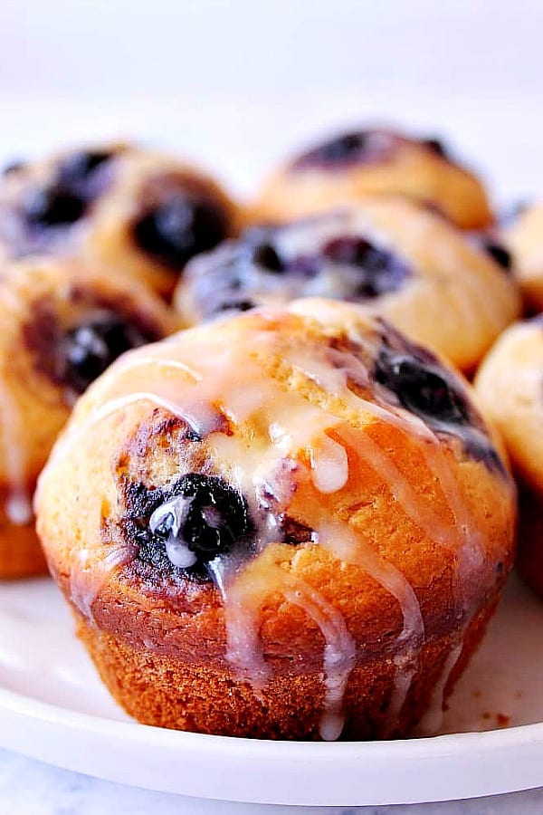 These perfect Blueberry Muffins are filled with sweet blueberries and drizzled with lemon glaze. Blueberry Muffins on a white plate.