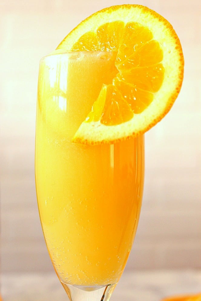 Orange Creamsicle Mimosa Recipe - refreshing and creamy cocktail that tastes just like a creamsicle! Quick and easy to make for your next party! close up of orange mimosa in glass with orange slice