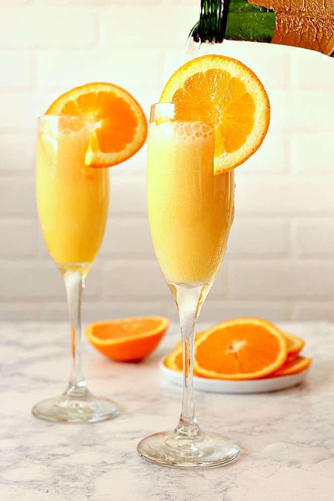 Orange Creamsicle Mimosa Recipe - refreshing and creamy cocktail that tastes just like a creamsicle! Quick and easy to make for your next party! pouring champagne into flute with orange juice and slices