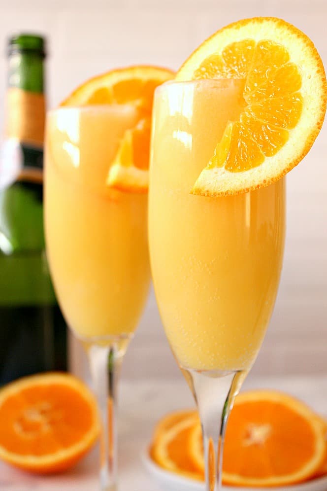 Orange Creamsicle Mimosa Recipe - refreshing and creamy cocktail that tastes just like a creamsicle! Quick and easy to make for your next party! orange mimosa with a slice of orange in champagne flute