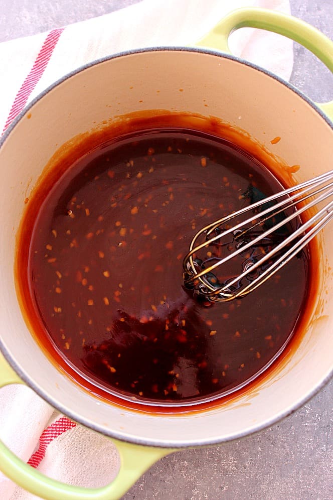 Teriyaki sauce in a cooking pot with a whisk.