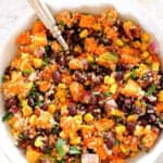 Sweet potato quinoa salad in a white bowl with a fork, on a gray board.