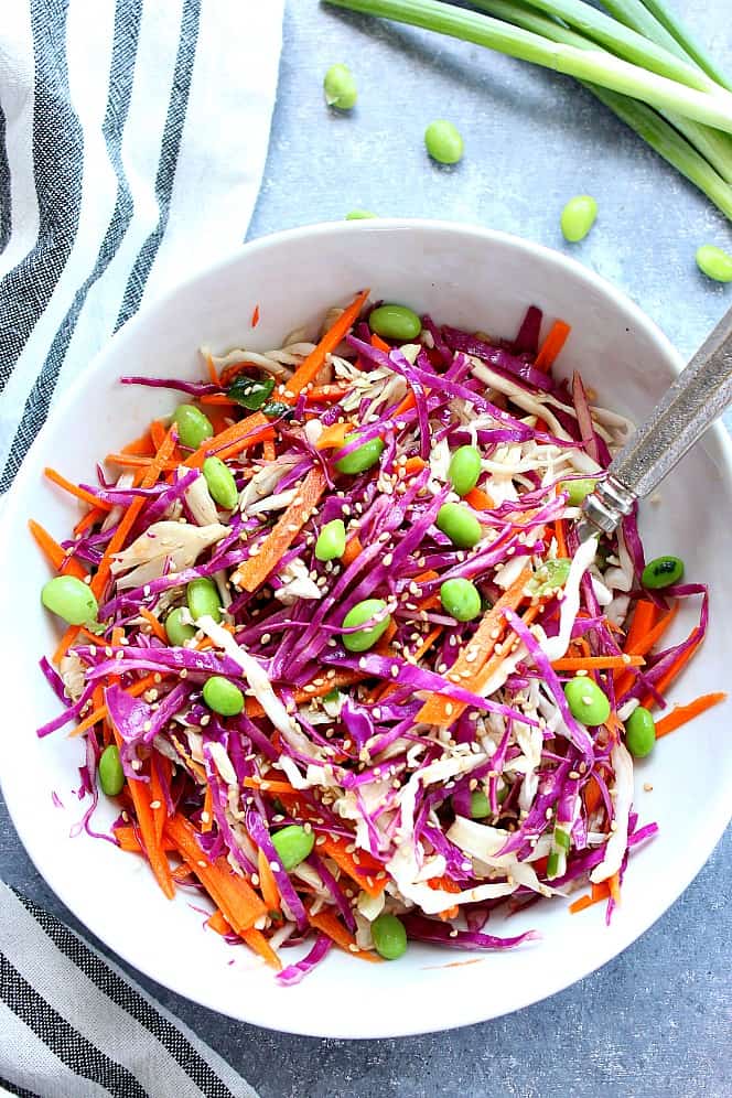 Overhead shot of Asian cabbage slaw with carrots and edamame in a white bowl. 