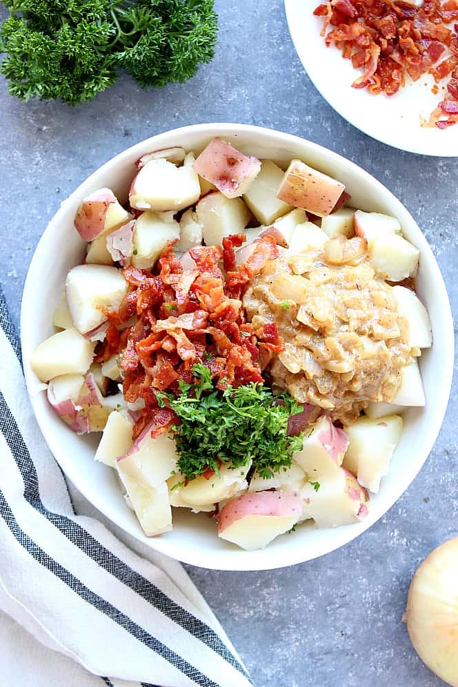 Cooked red potatoes, crispy bacon and mustard onion dressing in a white bowl with chopped parsley. 