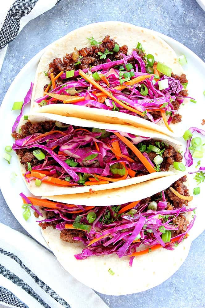 Three Korean Beef Tacos with Asian slaw on white plate. 