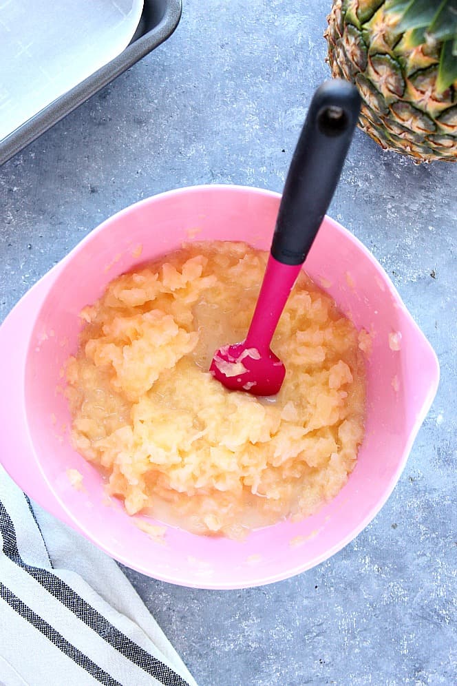 Crushed pineapple filling in pink mixing bowl with pink spatula. 