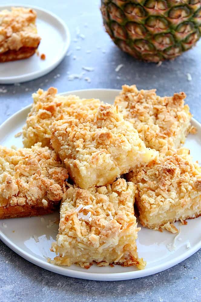 Pineapple coconut crumb bars served on plate, with fresh pineapple in the background. 
