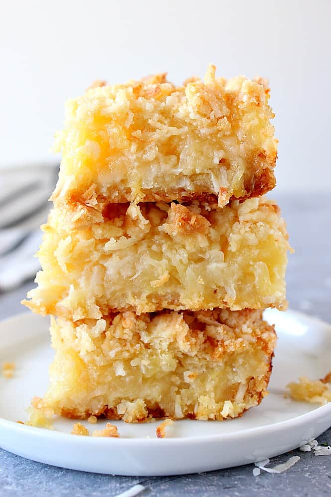 Pineapple Coconut Crumb Bars - easy, sweet and taste like tropical dessert. Crunchy coconut crumb topping and gooey pineapple filling make for irresistible combo! Close up on pineapple coconut bars stacked on white plate.
