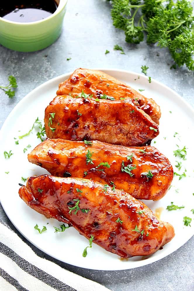 Sticky Asian Chicken on white plate, garnished with chopped parsley. 