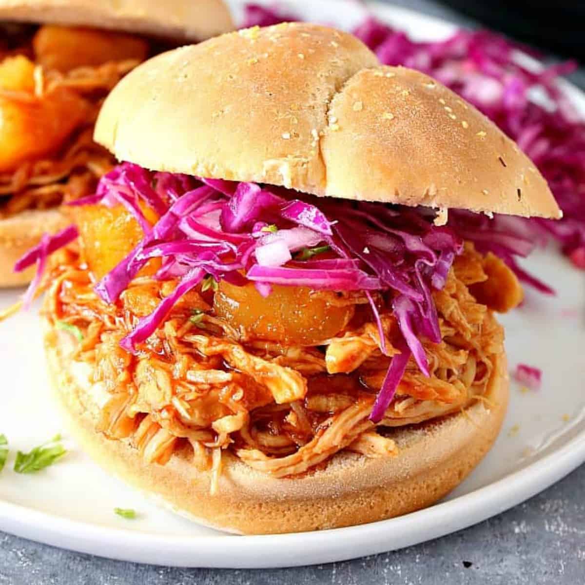 Pulled barbecue chicken in a bun on a plate.