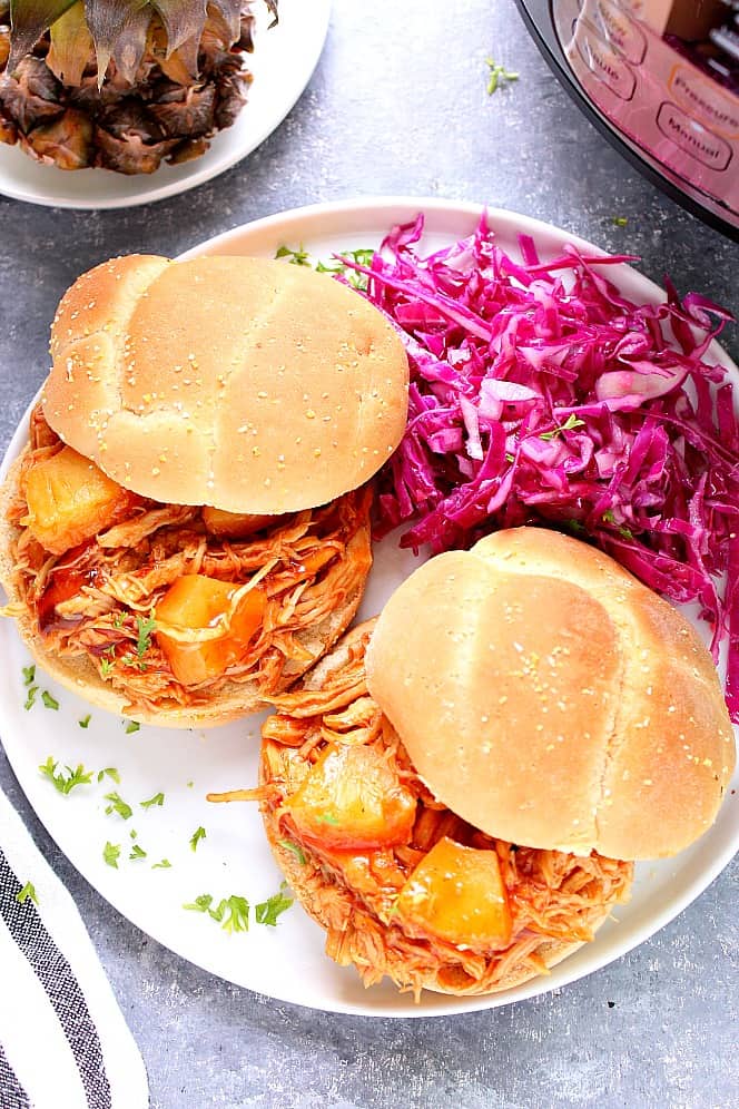 Two sandwiches with pulled BBQ chicken, purple cabbage coleslaw, served on white plate. 