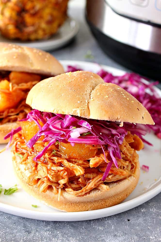 Pulled BBQ chicken in a bun with purple cabbage coleslaw, served on a white plate. 