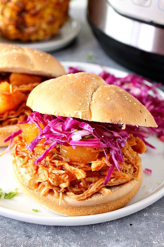 Instant Pot Hawaiian BBQ Chicken Recipe - pulled chicken with sweet pineapple BBQ sauce cooked in pressure cooker. Perfect served as sandwiches! Pulled BBQ chicken in a bun with purple cabbage coleslaw, served on a white plate.