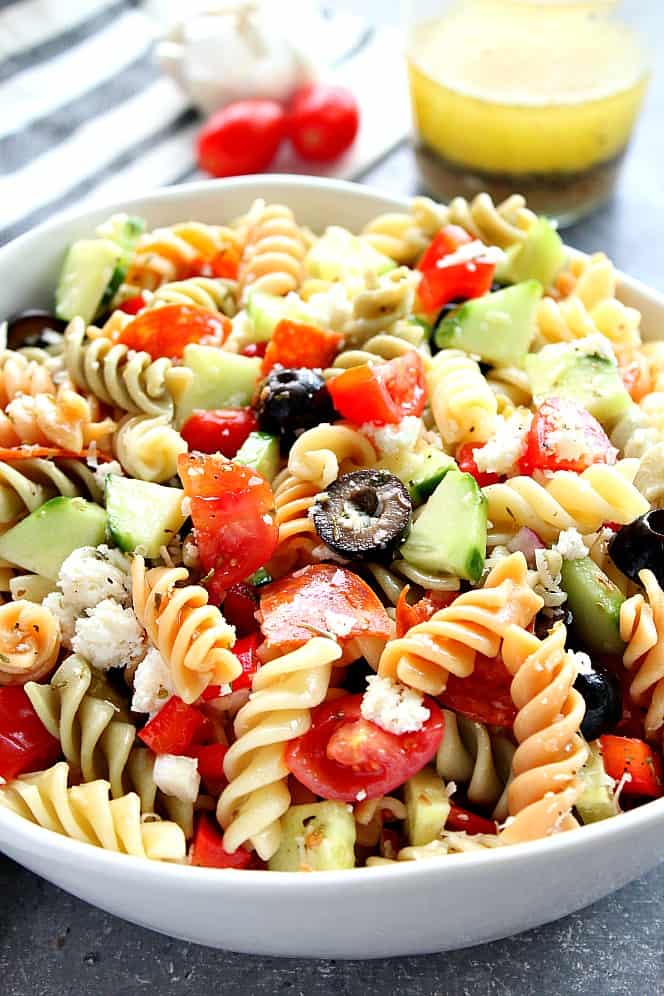 Close up on Italian Pasta Salad in white bowl, with homemade dressing in jar in the background. 