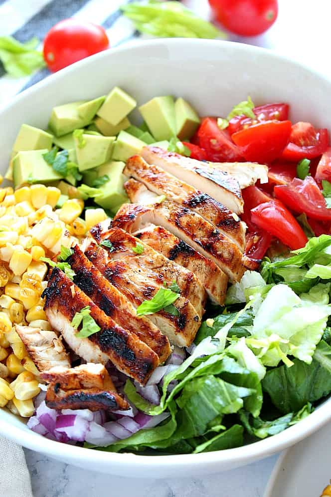 Side view shot of grilled chicken in white bowl, with lettuce, tomatoes and corn. 