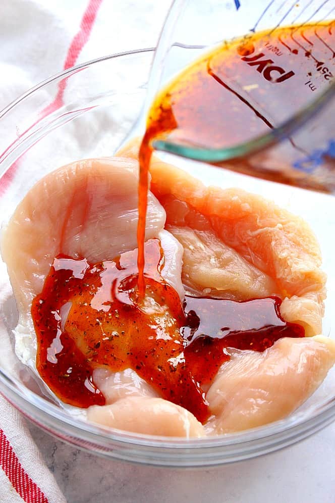 Close up shot of marinade being poured over chicken breast in bowl.