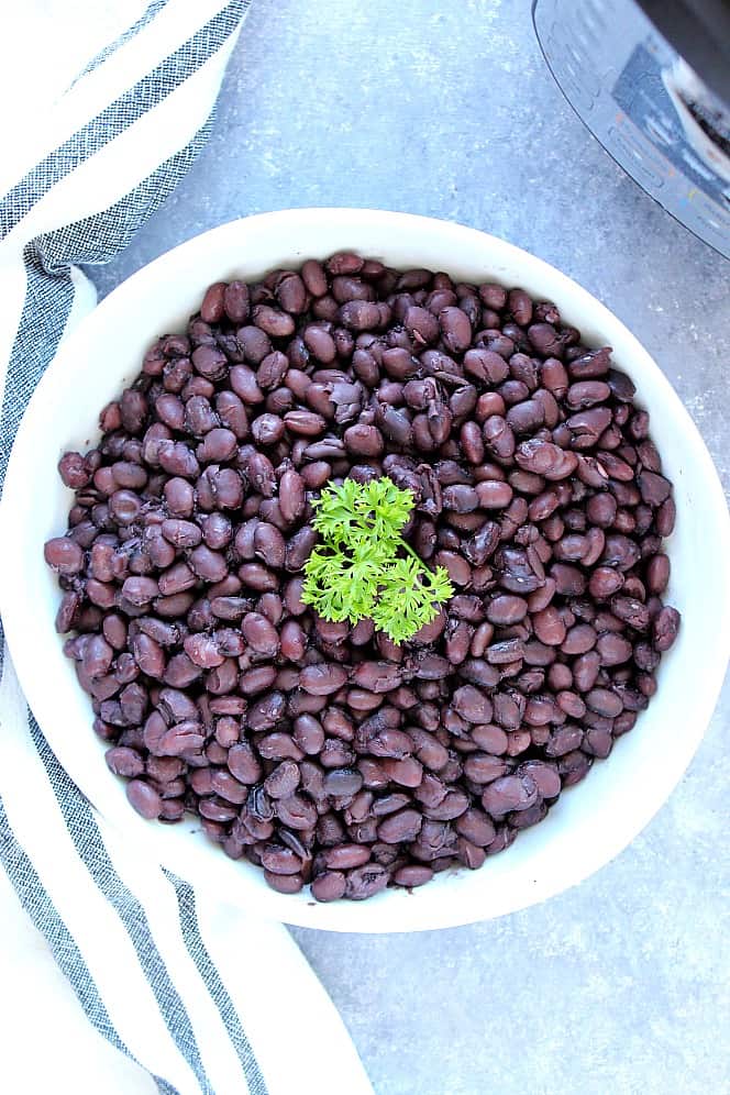 Overhead shot of black beans in white bowl with a sprig of parsley. 