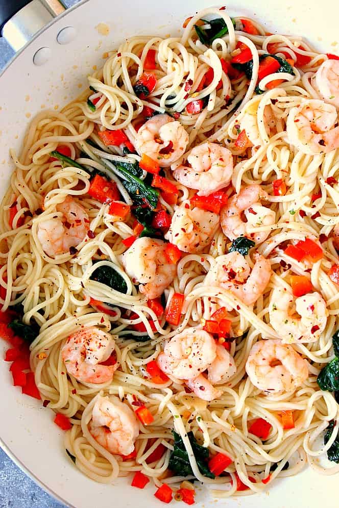 Shrimp Scampi with red peppers and spinach and Angel hair pasta in white cooking pan. 