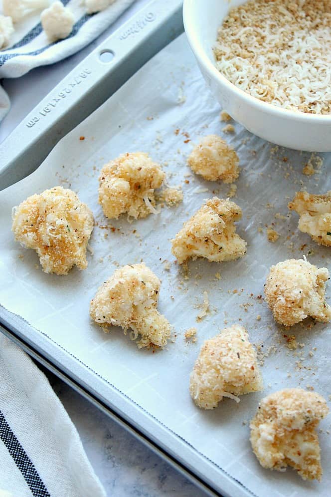 Roasted Garlic Parmesan Cauliflower Recipe - crispy cauliflower bites with garlic Parmesan breading, baked in the oven instead of fried. Side shot of breaded cauliflower florets on baking sheet.