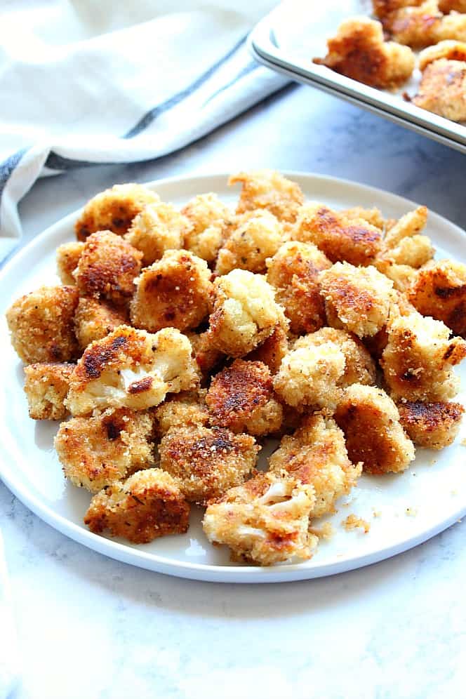 Roasted Garlic Parmesan Cauliflower Recipe - crispy cauliflower bites with garlic Parmesan breading, baked in the oven instead of fried. So tasty! Side shot of roasted breaded cauliflower bites on white plate.