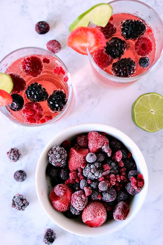 Overhead shot of frozen berries in white bowl with two glasses of sangria on the side.
