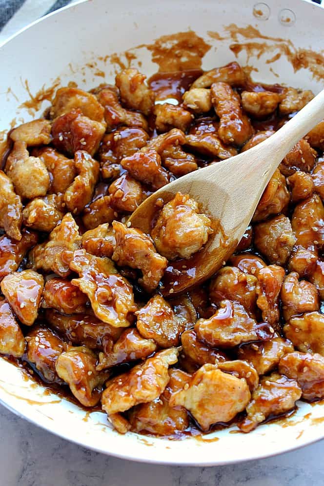 Side shot of battered chicken in sesame sauce in white pan. 