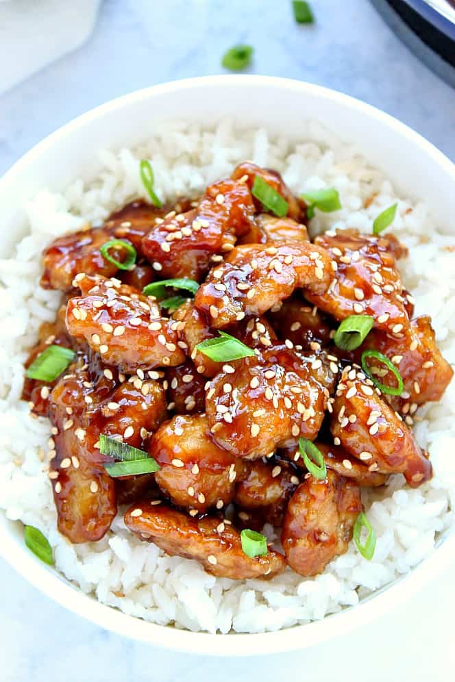 Overhead shot of sesame chicken served on white rice in white bowl. 