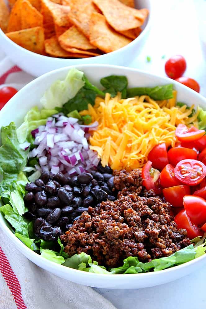 Side shot of ingredients for taco salad in white bowl. 