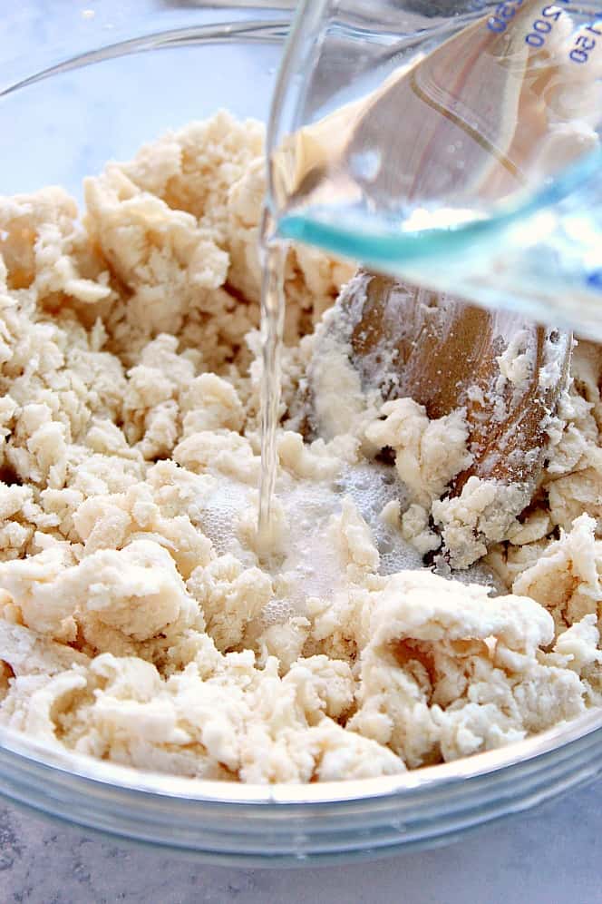 Close up shot of biscuit dough in a glass bowl, with soda poured from measuring cup.