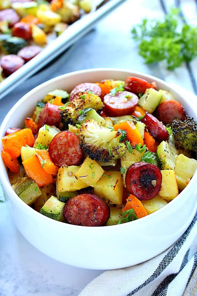 Side shot of white bowl filled with roasted sausage and vegetables. 