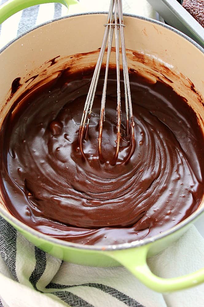 Overhead shot of rich fudgy chocolate frosting in saucepan, with whisk on the side.