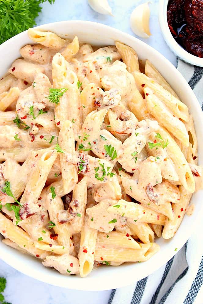 Overhead shot close up of creamy sun-dried Alfredo pasta with chicken, in white bowl. 