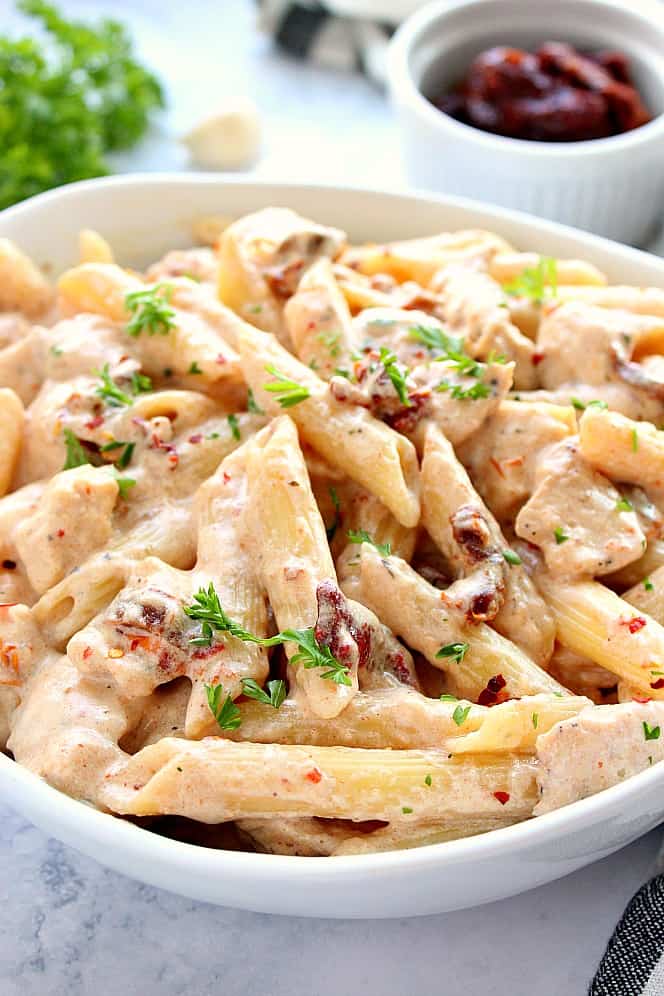 Close up side shot of creamy pasta with chicken and sun-dried tomato Alfredo sauce, garnished with chopped parsley.