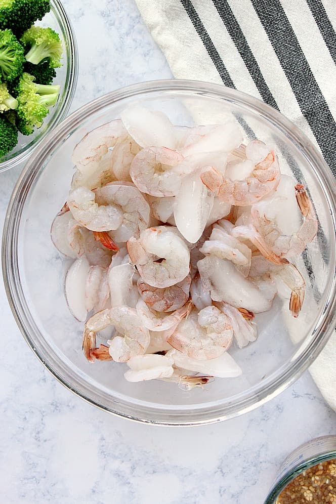 Overhead shot of raw medium shrimp with ice in a glass bowl.