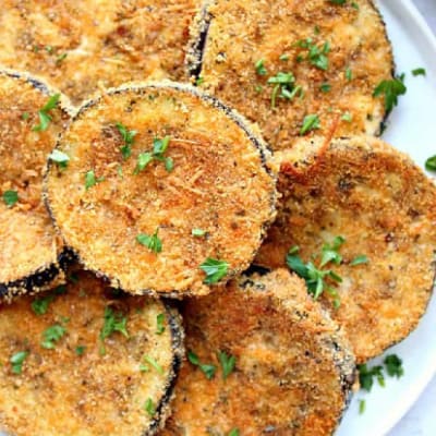 Square image of baked crispy eggplant on a white plate.