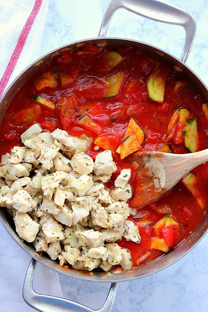 Overhead shot of saucy ratatouille in skillet with season chicken added. 