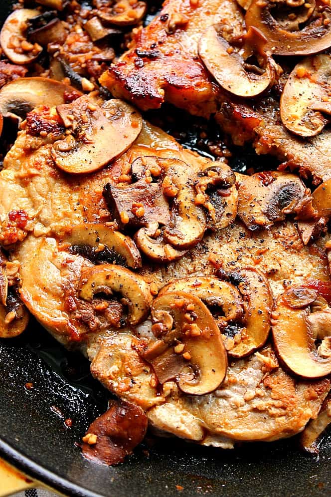 Close up overhead shot of seared pork chops with mushrooms in cast iron skillet.