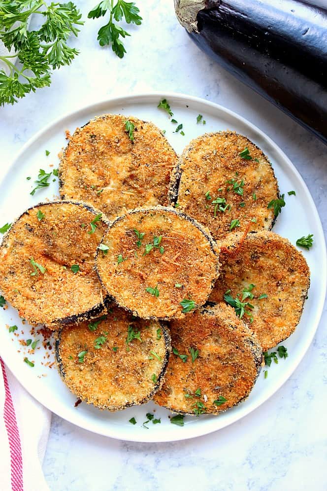 Overhead shot of baked crispy eggplant on white serving plate, garnished with chopped parsley. 