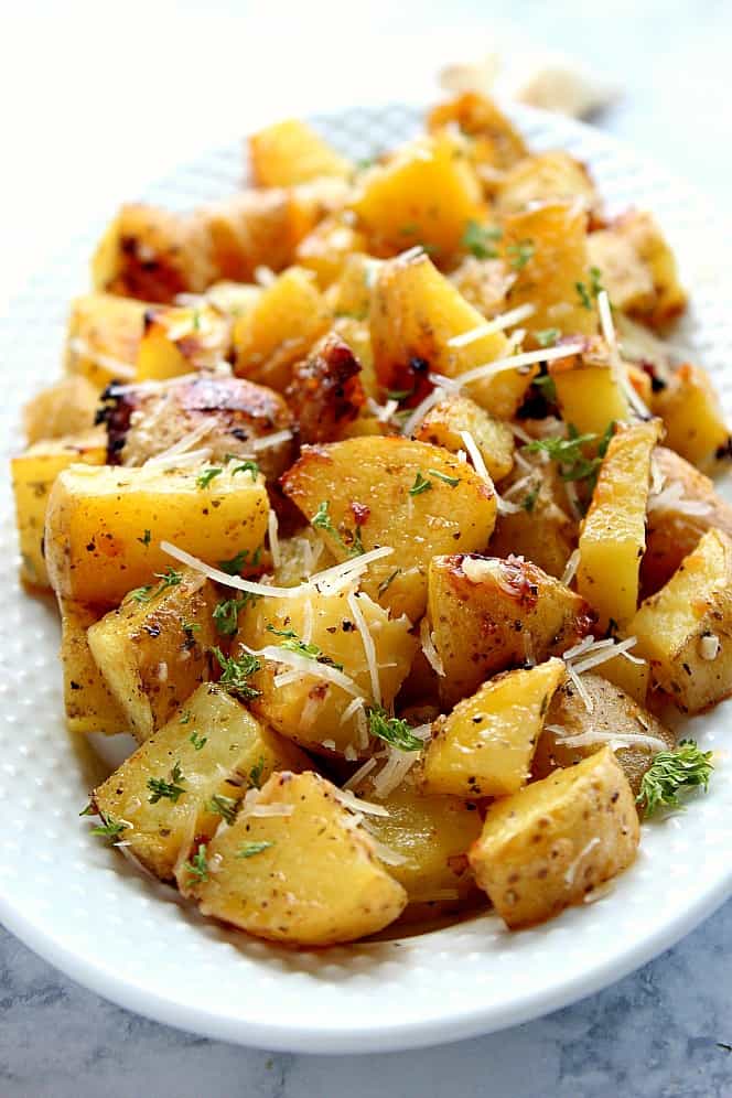 Roasted potatoes with Parmesan cheese and chopper parsley on white serving bowl.