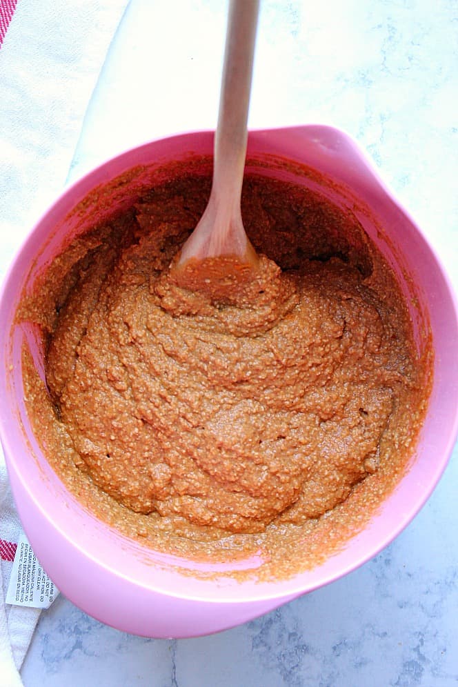 Overhead shot of pumpkin muffin batter in pink mixing bowl, with wooden spoon.