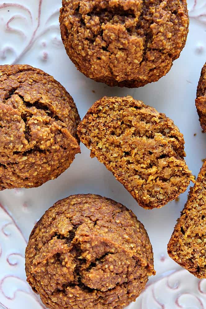 Overhead shot of healthy pumpkin muffins on white plate, one muffin cut through. 