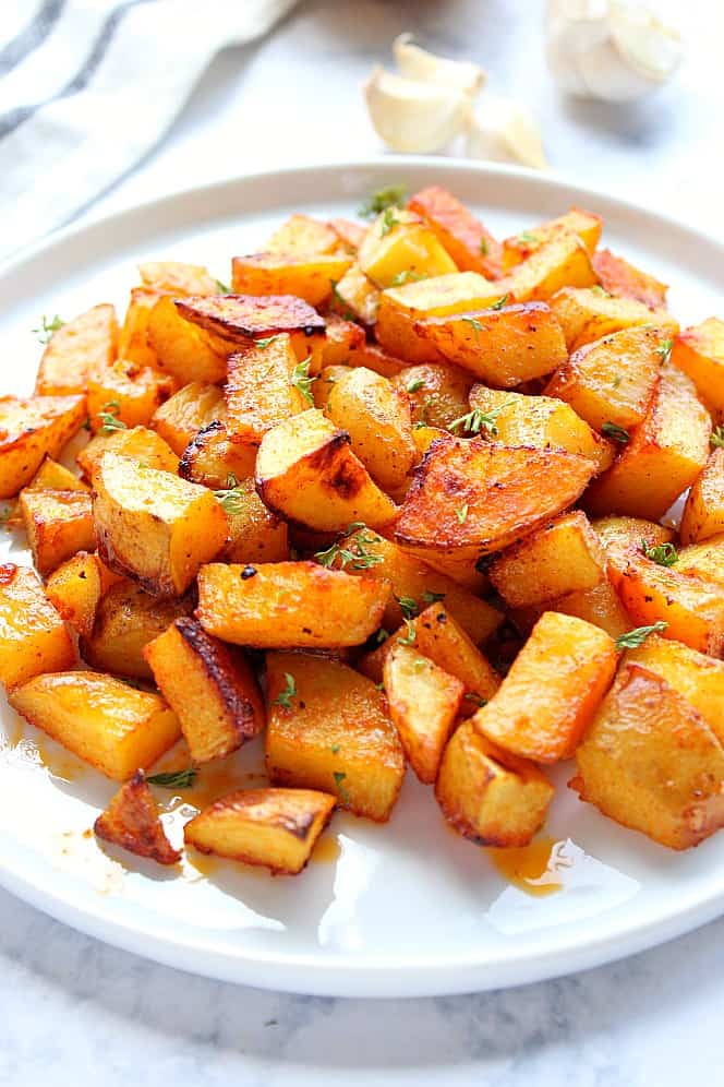 Side shot of golden roasted potatoes on white plate, garnished with parsley. 
