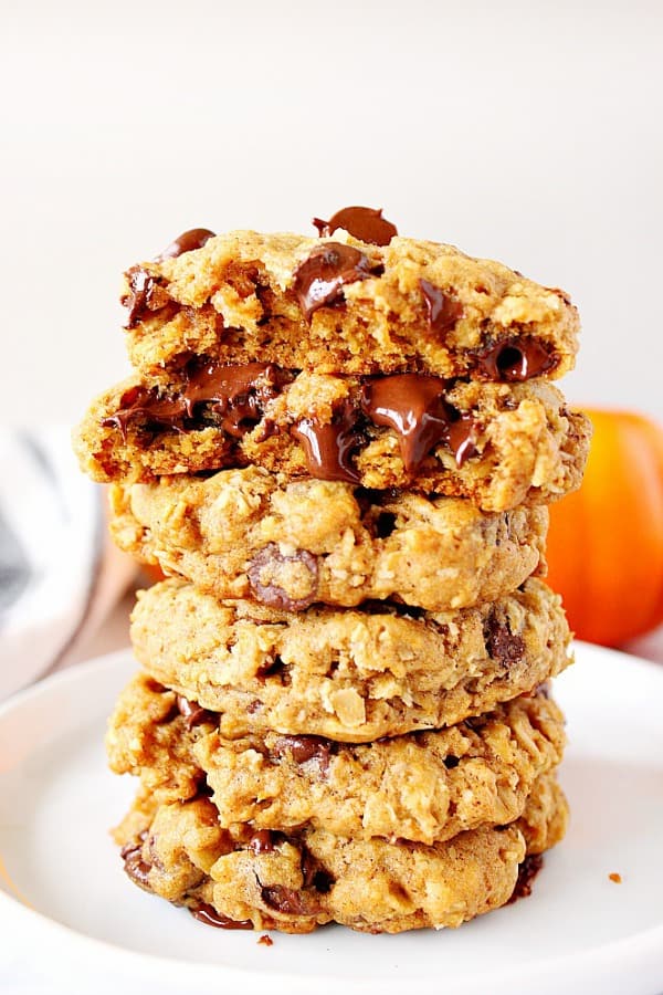 Pumpkin Oatmeal Chocolate Chip Cookies Recipe - easy, chewy oatmeal cookies with pumpkin, spices and chocolate chips. No mixer needed! Five pumpkin oatmeal cookies stacked up on each other on a white plate.
