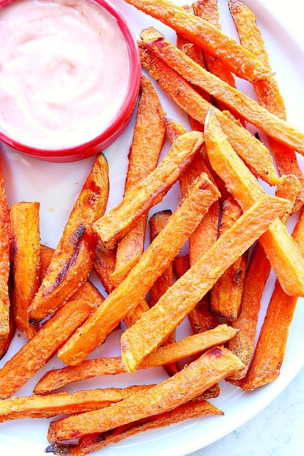 Baked sweet potato fries on white plate, with red bowl with dip.