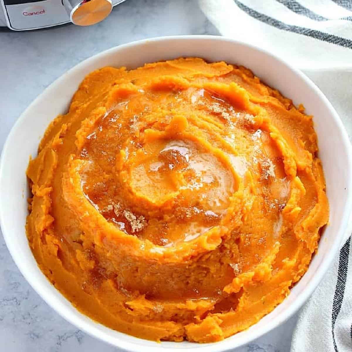 Square image of sweet potatoes mashed in a white bowl next to the Instant Pot.