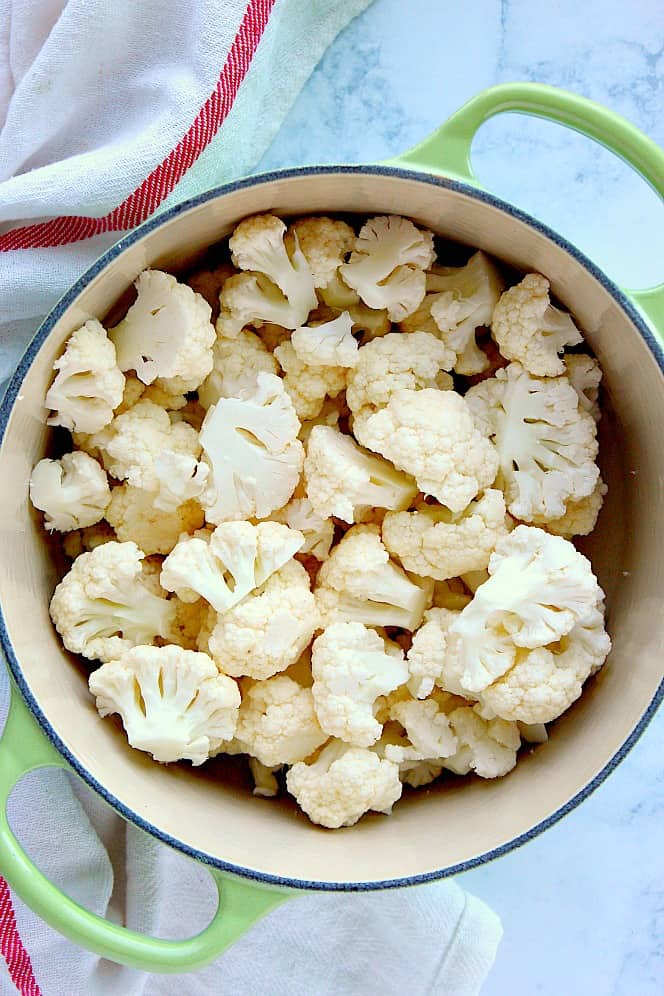 Overhead shot of cauliflower florets in green cooking pot. 