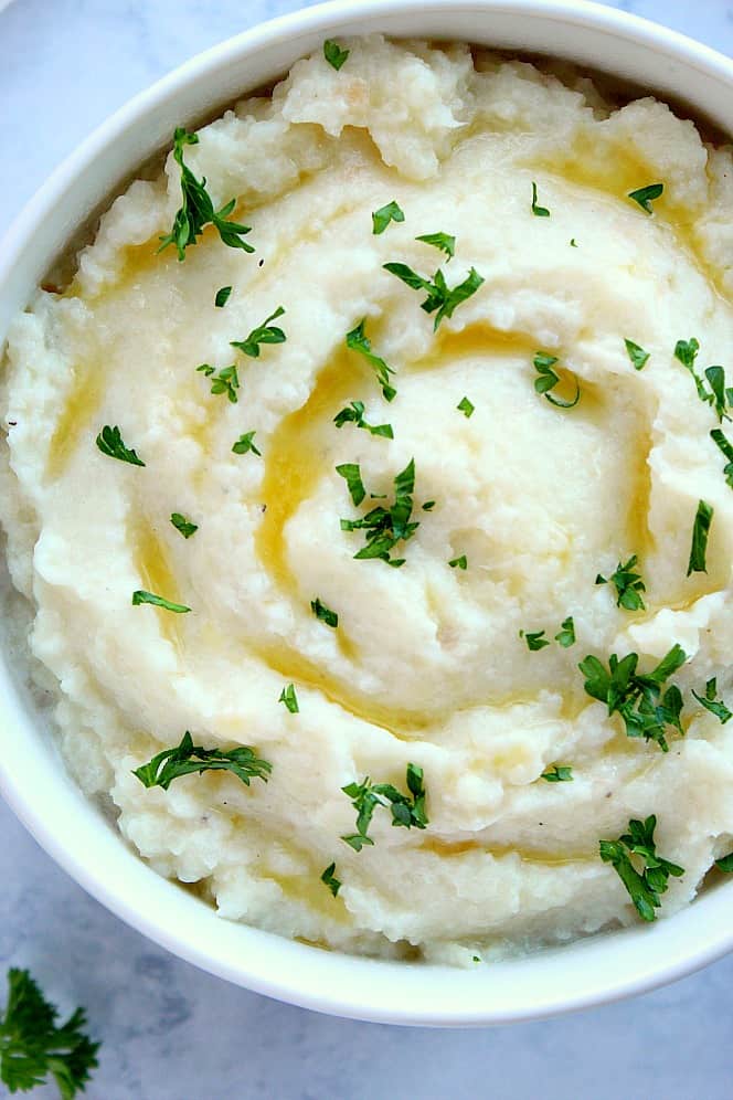 Overhead shot of mashed cauliflower in serving bowl. Garnished with chopper parsley.