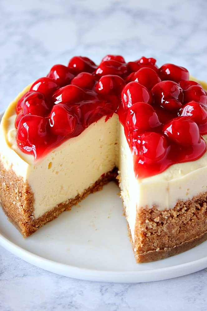 Close up shot of cheesecake with cherry topping, with one slice missing. 